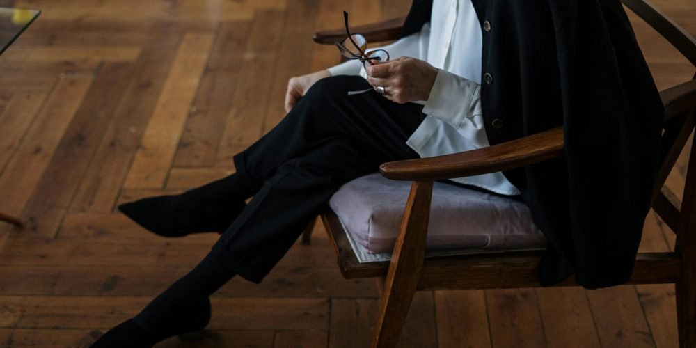A woman holding glasses, seated indoors, exuding professionalism and calm.